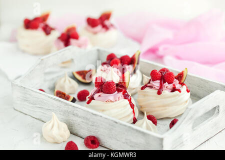 Delizioso mini pavlova meringa torta decorata con lamponi freschi, fichi e salsa di frutti di bosco su sfondo bianco Foto Stock