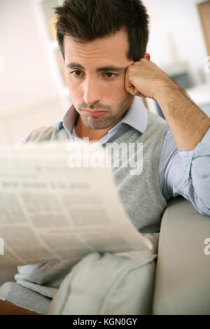 Uomo seduto in divano e la lettura di cattive notizie Foto Stock
