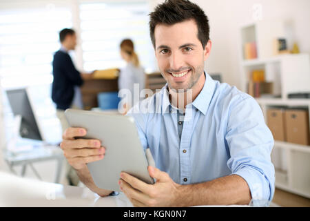 Uomo sorridente in ufficio a lavorare sulla tavoletta digitale Foto Stock