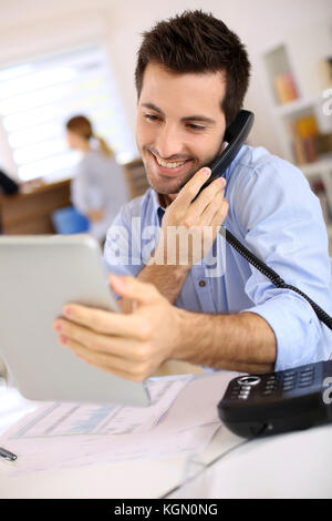 Uomo sorridente in ufficio a rispondere al telefono Foto Stock