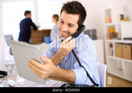 Uomo sorridente in ufficio a rispondere al telefono Foto Stock