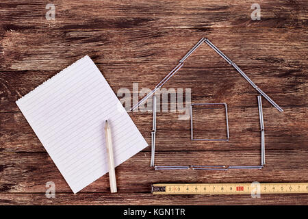Home concetto. modello in legno casa su di un tavolo di lavoro con strumenti e vuoto per notebook a spirale Foto Stock