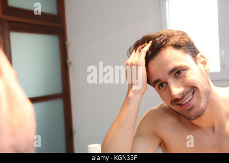 Giovane uomo guardando i capelli in specchio Foto Stock