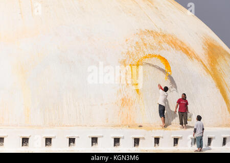 Gli uomini di gettare un arancio il lavaggio Stupa Boudhanath nella valle di Kathmandu, Nepal Foto Stock