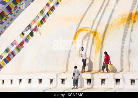 Gli uomini di gettare un arancio il lavaggio Stupa Boudhanath nella valle di Kathmandu, Nepal Foto Stock