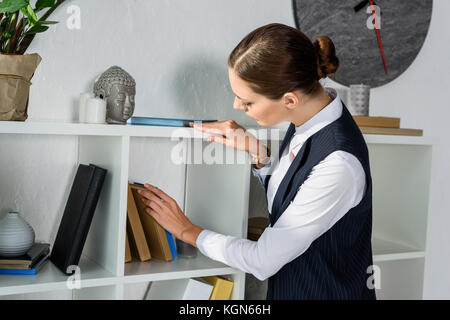 Imprenditrice guardando libri sullo scaffale Foto Stock