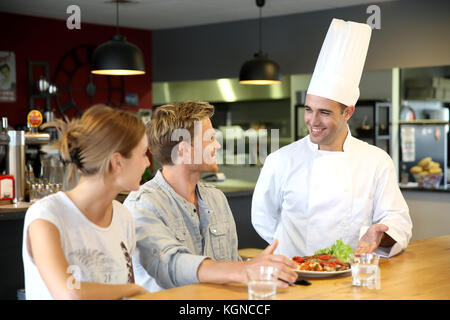 Il giovane chef servire piatto cucinato per i clienti Foto Stock