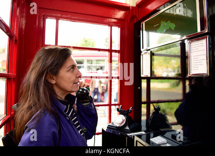 Femmina residente locale utilizzando un tradizionale telefono rosso scatola che è stato convertito in un piccolo centro visitatori. l'interno della casella telefono dispone ora di un Foto Stock