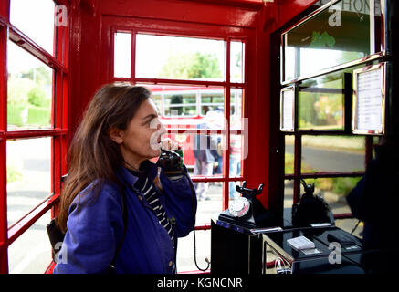 Femmina residente locale utilizzando un tradizionale telefono rosso scatola che è stato convertito in un piccolo centro visitatori. l'interno della casella telefono dispone ora di un Foto Stock