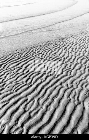 Immagine in bianco e nero della linea costiera inferiore increspata quando le prime increspature della marea in arrivo avanzano. Creste fluviali per studio di stratigrafia. Foto Stock