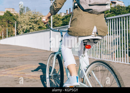 Donna in camicia e jeans vanno in bicicletta intorno alla città una giornata di sole Foto Stock