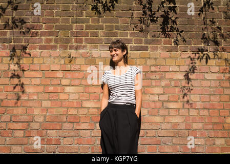 Giovane Donna vestita di urbano in stile minimale con il bianco e nero a strisce maglietta e pantaloni neri. Un muro di mattoni come sfondo Foto Stock