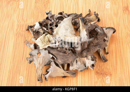 Pila di prima classe essiccato corno dell'abbondanza di funghi su scuro di bambù tagliere di legno Foto Stock