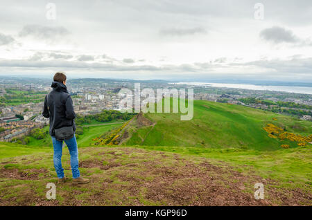 Giovani modello femminile ammirando il paesaggio di Edimburgo dalla sommità del Arthur Seat. Scozia, Regno Unito. Foto Stock