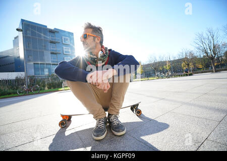 Alla moda ragazzo seduto su skateboard in posizione di parcheggio Foto Stock