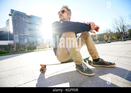 Alla moda ragazzo seduto su skateboard in posizione di parcheggio Foto Stock