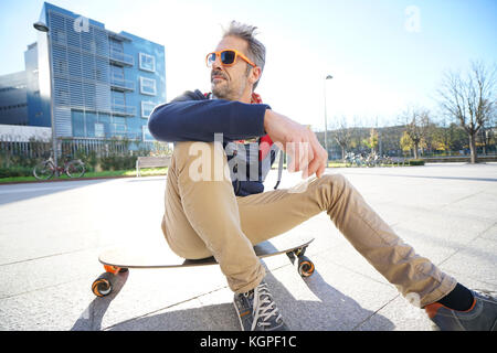 Alla moda ragazzo seduto su skateboard in posizione di parcheggio Foto Stock