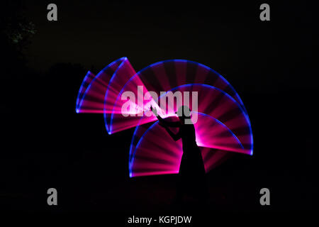Vista laterale, silhouette nera della femmina isolato in hat in piedi all'aperto durante la notte, ponendo le braccia davanti con magic rosa effetto di luce dietro. Foto Stock