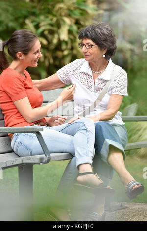 Senior donna con accompagnatore seduta sul banco di lavoro presso il parco Foto Stock