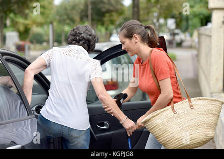 Giovane badante aiutando donna senior di arrivare in auto Foto Stock