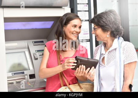 Home caregiver e donna disabile ottenere contanti dalla banca Foto Stock