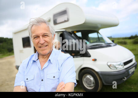 Ritratto di felice senior uomo in piedi nella parte anteriore del motorhome Foto Stock