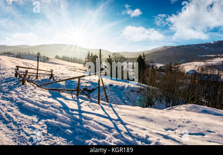 Recinzione rotto su un pendio nevoso nelle zone rurali sono. incantevole paesaggio invernale con il sole luminoso sulla cresta della montagna Foto Stock
