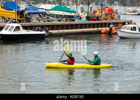 Kayakers tandem paddling in Falmouth Harbour, UK con quayside e barche in background Foto Stock