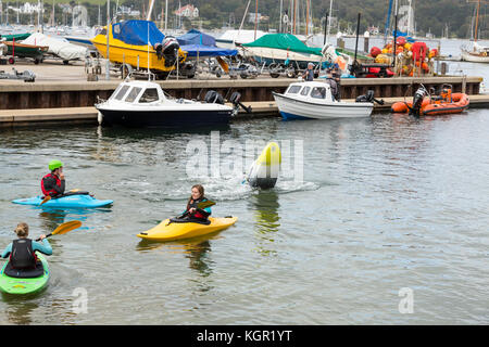 Giovani kayakers formazione in Falmouth Harbour, UK con quayside e barche in background. istruttore dimostrando eskimo roll Foto Stock