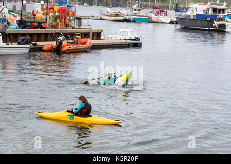 Giovani kayakers formazione in Falmouth Harbour, UK con quayside e barche in background. istruttore dimostrando eskimo roll Foto Stock