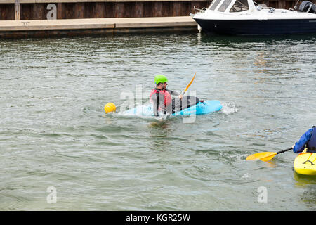 Giovani kayakers formazione in Falmouth Harbour, UK con quayside e barche in background. istruttore dimostrando eskimo roll Foto Stock