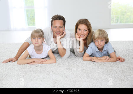 La famiglia felice di quattro la posa su un tappeto a casa Foto Stock