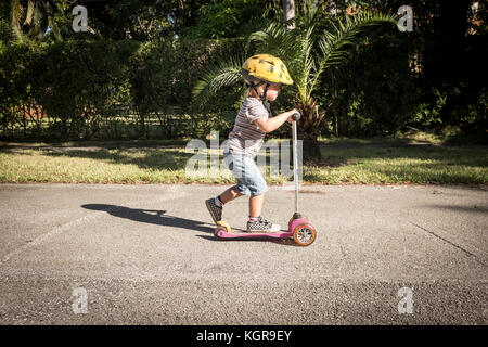 Un giovane di 3 anno vecchio ragazzo gioca sul suo scooter Foto Stock