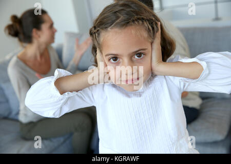 Bambina che copre i suoi orecchi per non udire i genitori sostenendo Foto Stock