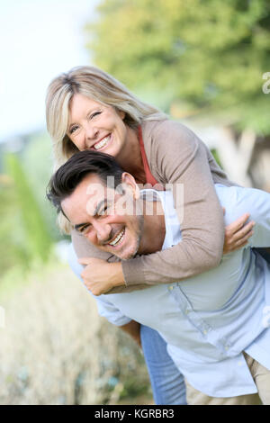 Allegro uomo maturo dando piggyback ride per donna Foto Stock