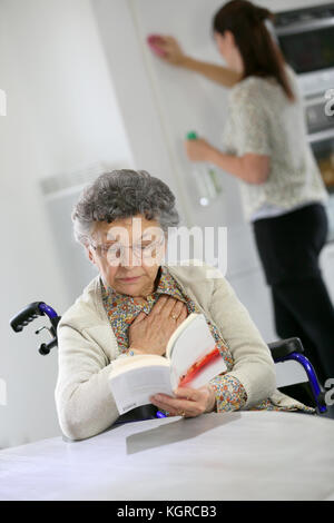 Donna anziana libro, home helper in background Foto Stock