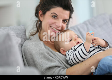 Allegro madre cuddling in divano con baby figlio Foto Stock