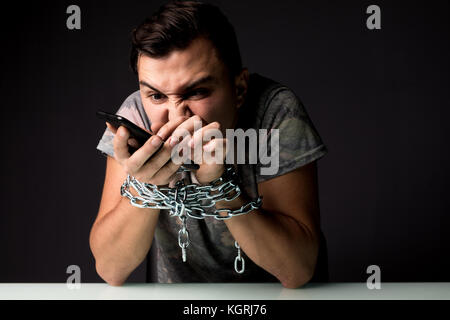 Giovane uomo che soffrono di dipendenza dal telefono dipendenza digitando su screan con catena sulle mani Foto Stock