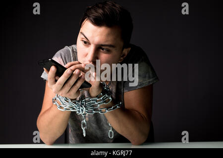 Giovane uomo che soffrono di dipendenza dal telefono dipendenza digitando su screan con catena sulle mani Foto Stock