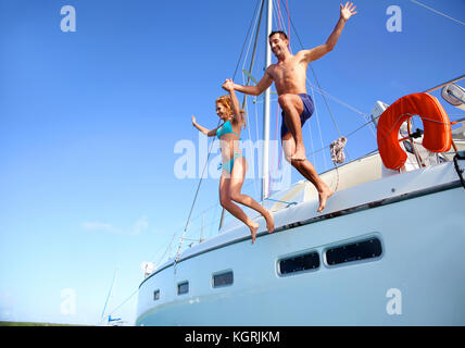 Coppia giovane saltando in acqua dalla barca Foto Stock