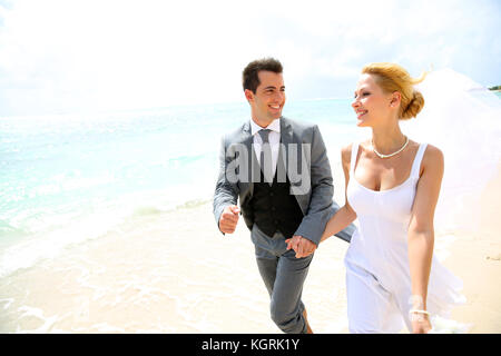 Appena una coppia sposata in esecuzione su di una spiaggia di sabbia Foto Stock