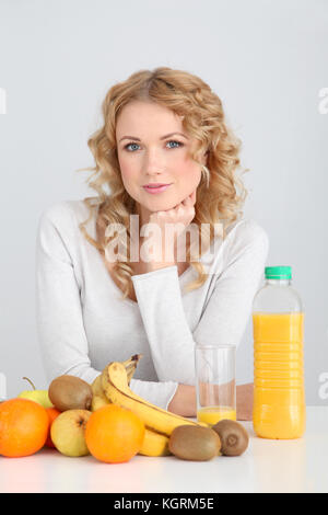 Sorridente donna bionda seduta con frutti sul tavolo Foto Stock