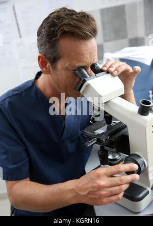 Medico nel laboratorio di ricerca attraverso il microscopio Foto Stock