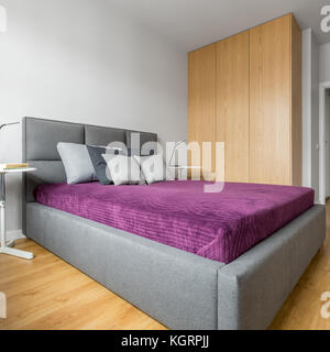 Camera da letto progettato in stile minimalista con grande letto grigio e alta armadio in legno Foto Stock