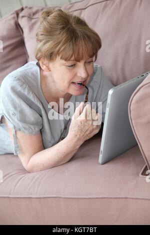 Donna senior con tavoletta elettronica a casa Foto Stock
