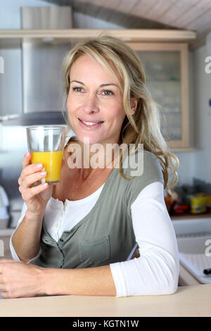 Ritratto di donna bionda in cucina a bere il succo d'arancia Foto Stock