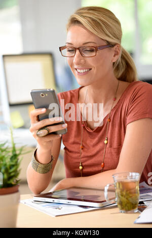 La donna di casa-ufficio utilizza lo smartphone Foto Stock