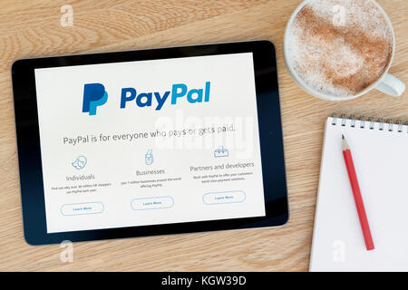 Il sito web di PayPal funzioni su un iPad dispositivo tablet pc che si appoggia su una tavola di legno accanto a un blocco note e matita e una tazza di caffè (solo uso editoriale Foto Stock