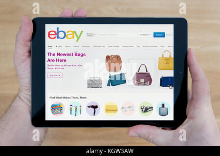 Un uomo guarda il sito Web di eBay sul suo iPad dispositivo tablet, sparato contro un tavolo di legno top sfondo (solo uso editoriale) Foto Stock