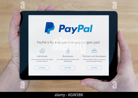 Un uomo guarda al sito web di Paypal sul suo iPad dispositivo tablet, sparato contro un tavolo di legno top sfondo (solo uso editoriale) Foto Stock